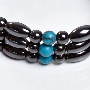 May include: A bracelet made of black hematite and turquoise beads. The bracelet has three rows of hematite beads and two turquoise beads in the center.