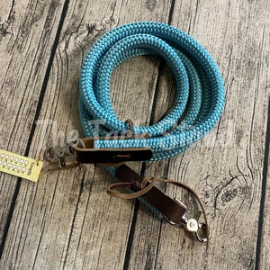 May include: A coiled turquoise rope with leather accents and metal clasps. The rope is made of a thick, braided material. A small tag with text is attached. The rope is likely used for equestrian purposes.