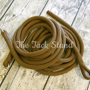 May include: A brown braided rope lead with two silver snap hooks. The lead is coiled on a wooden surface.