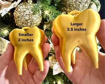 May include: Two gold tooth-shaped ornaments, one larger than the other. The larger ornament is 3.5 inches tall and the smaller ornament is 2 inches tall.
