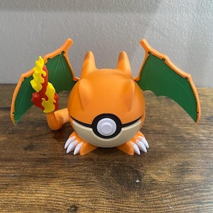 May include: An orange Charizard figure with green wings and a flame tail. The figure has white claws and a black and white eye. The figure is a collectible item.
