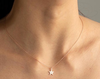 May include: A delicate gold chain necklace with a small star pendant. The necklace is worn by a person with a black tank top.