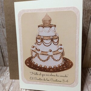 Könnte beinhalten: Eine weiße Hochzeitstorte mit braunem Frosting und Schokoladenakzenten. Die Torte ist mit Perlen, Herzen und einem kleinen Cupcake verziert. Der Text "Hallé al que mi alma ha amado. El Cantar de los Cantares 3:4" ist unter der Torte gedruckt.