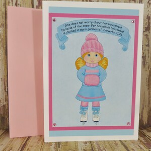 May include: A pink and blue card with a girl wearing a pink hat, blue coat, and pink mittens. The card has a quote from Proverbs 31:21, "She does not worry about her household because of the snow, For her whole household is clothed in warm garments."