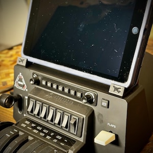 Op de afbeelding: Een zwart bedieningspaneel voor een vluchtsimulator met een aangesloten tablet. Het paneel heeft tal van schakelaars, draaiknoppen en hendels, waaronder een klepbediening en de tekst "HONEYCOMB AEROSPACE". De tablet zit in een beschermhoes.