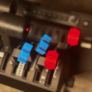 May include: Close-up of a black control panel with multiple red and blue toggle switches. The switches are arranged in a row and have a textured surface.