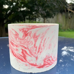 Könnte beinhalten: Zylindrischer Pflanztopf mit weißer Basis und rotem Marmormuster. Der Pflanztopf besteht aus Beton und ist für den Innen- und Außenbereich geeignet. Der Pflanztopf hat einen Durchmesser von ca. 12 cm und ist 10 cm hoch.