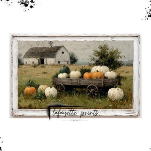 Op de afbeelding: Een ingelijste print toont een rustieke herfstsc&egrave;ne. Een schuur met een ster staat op de achtergrond. Een houten kar is gevuld met pompoenen in verschillende kleuren. De print wordt omgeven door een witte, verweerde lijst.