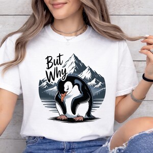 Könnte beinhalten: Weißes T-Shirt mit einer Illustration eines traurigen Pinguins und dem Text "But Why". Der Pinguin ist schwarz und weiß, vor dem Hintergrund von Bergen und blauem Himmel. Ein lässiges Kleidungsstück für den Alltag.