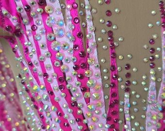 Peut inclure: Un justaucorps doté d'un corsage en maille couleur chair orné de rayures verticales en tissu rose vif et rose clair. Le vêtement est richement décoré de nombreux cristaux iridescents et rose foncé disposés en motifs le long des rayures.