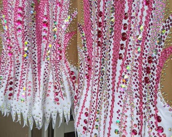 Peut inclure: Deux justaucorps sans manches avec un haut en maille couleur chair et une partie inférieure blanche. Les vêtements sont richement ornés d'un motif rayonnant de cristaux roses et irisés, créant un aspect vibrant, texturé et étincelant.