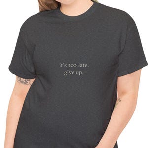 Camiseta minimalista con el lema "Es demasiado tarde, ríndete", diseño de meme con humor negro.