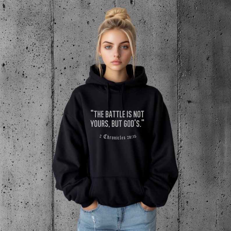 A Christian hoodie with the Bible verse The battle is not yours, but Godfrom 2 Chronicles 20:15 printed on the front. Suitable for religious individuals seeking faith-inspired apparel. Perfect for comfort, spirituality, and motivational reminders.