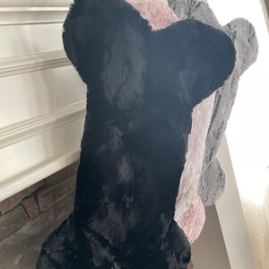 May include: Three plush dog bone stockings hanging from a fireplace mantel. The stockings are black, pink, and gray.