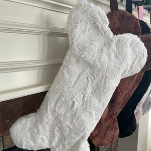 May include: White faux fur stocking shaped like a bone hanging on a fireplace mantel.