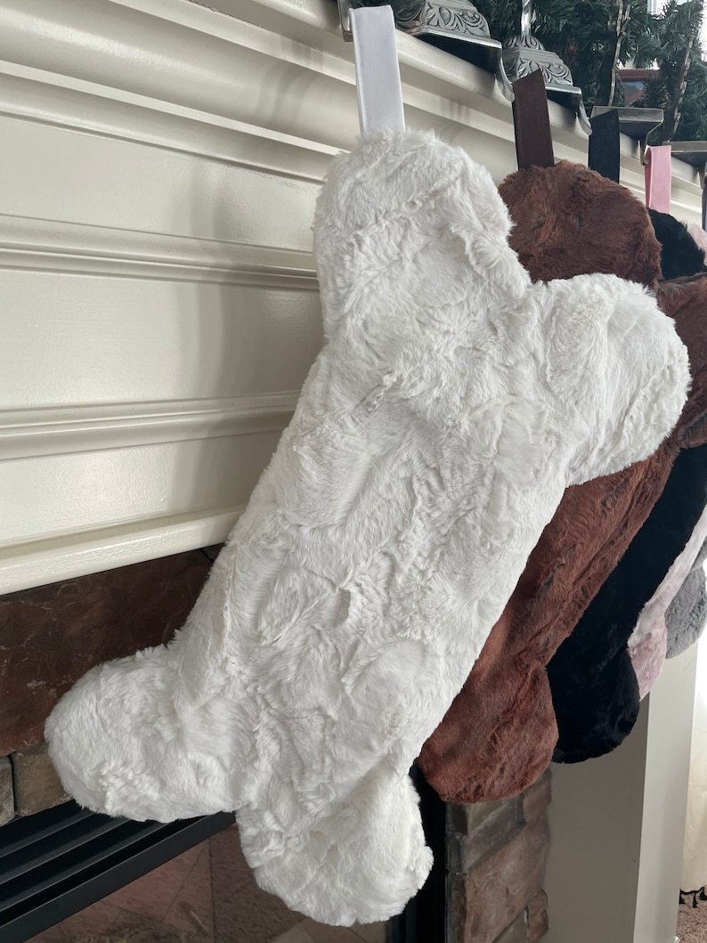 May include: White faux fur stocking shaped like a bone hanging on a fireplace mantel.