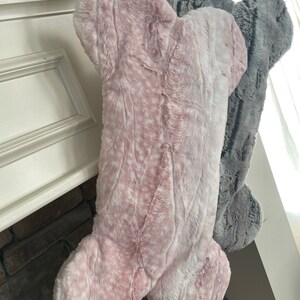 May include: Two plush dog bone stockings, one pink and one gray, hanging from a fireplace mantel.