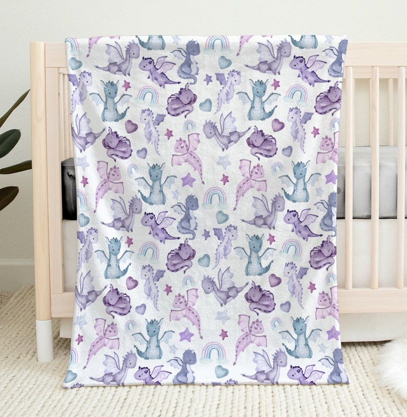 May include: A soft, white baby blanket with a repeating pattern of purple and blue watercolor dragons, stars, hearts, and rainbows.