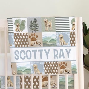May include: A baby crib sheet with a patchwork design featuring images of dogs, paw prints, trees, and mountains. The sheet has the name "SCOTTY RAY" in large, light blue letters across the center.