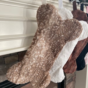 May include: A set of four plush dog bone stockings in brown, white, black, and pink. The stockings are hanging from a fireplace mantel.