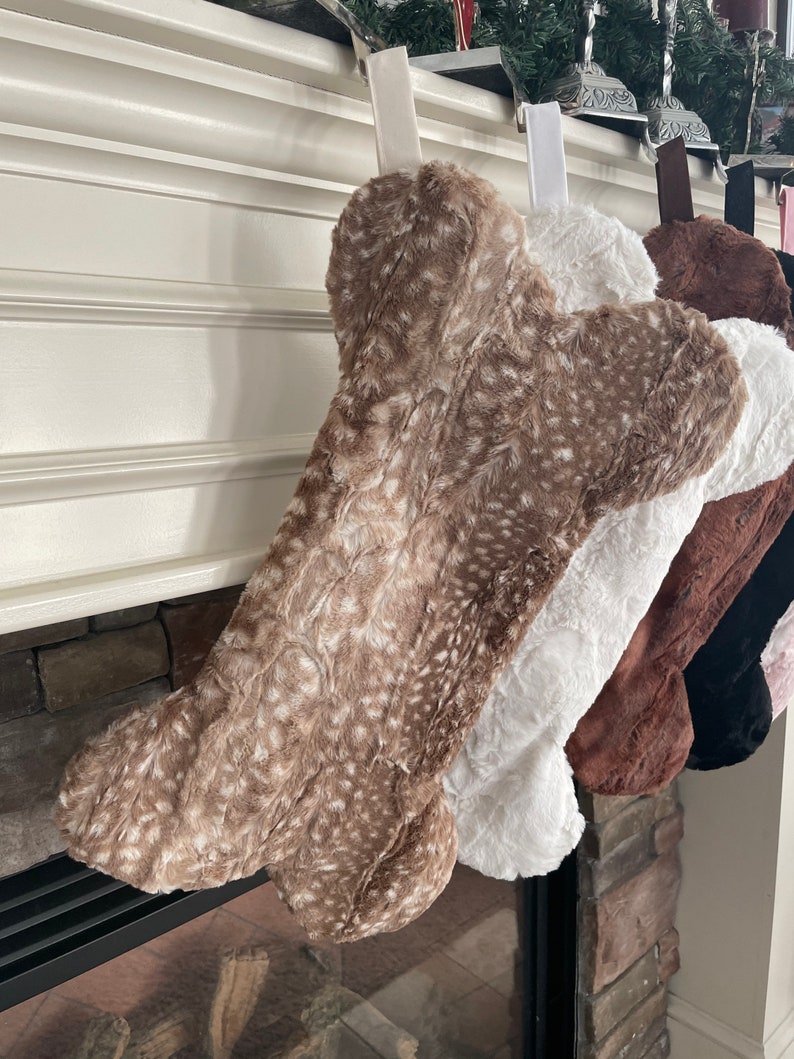 May include: A set of four plush dog bone stockings in brown, white, black, and pink. The stockings are hanging from a fireplace mantel.
