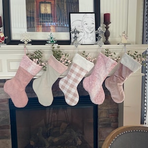 May include: Five pink and white Christmas stockings with white fur trim hanging on a fireplace mantel. The stockings are decorated with different patterns, including plaid, polka dots, and quilted.