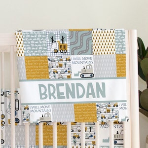 May include: A cot bumper with a construction theme. The bumper features a patchwork design with images of trucks, roads, and traffic cones in shades of grey, yellow, and blue. The name "BRENDAN" is displayed prominently.