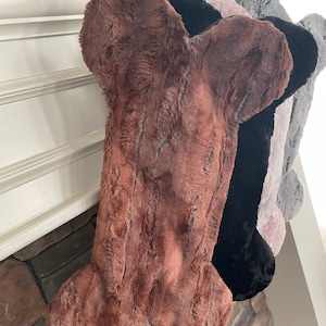 May include: Four faux fur bone-shaped stockings in brown, black, pink, and gray hanging on a fireplace mantel.