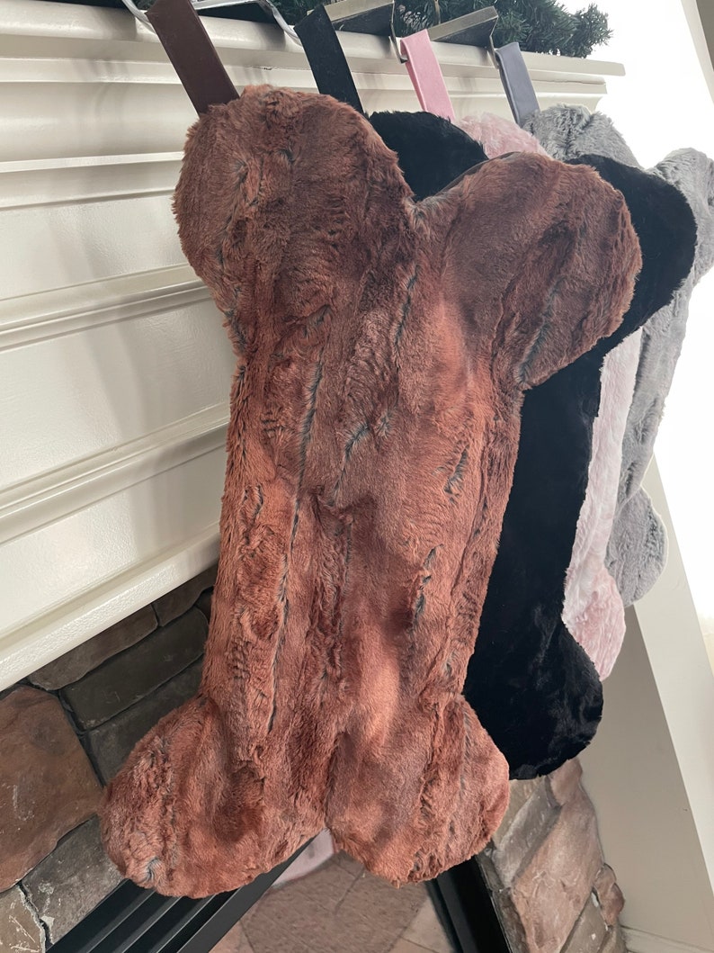 May include: Four faux fur bone-shaped stockings in brown, black, pink, and gray hanging on a fireplace mantel.