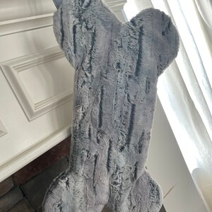 May include: A gray faux fur dog bone stocking hanging on a fireplace mantel.