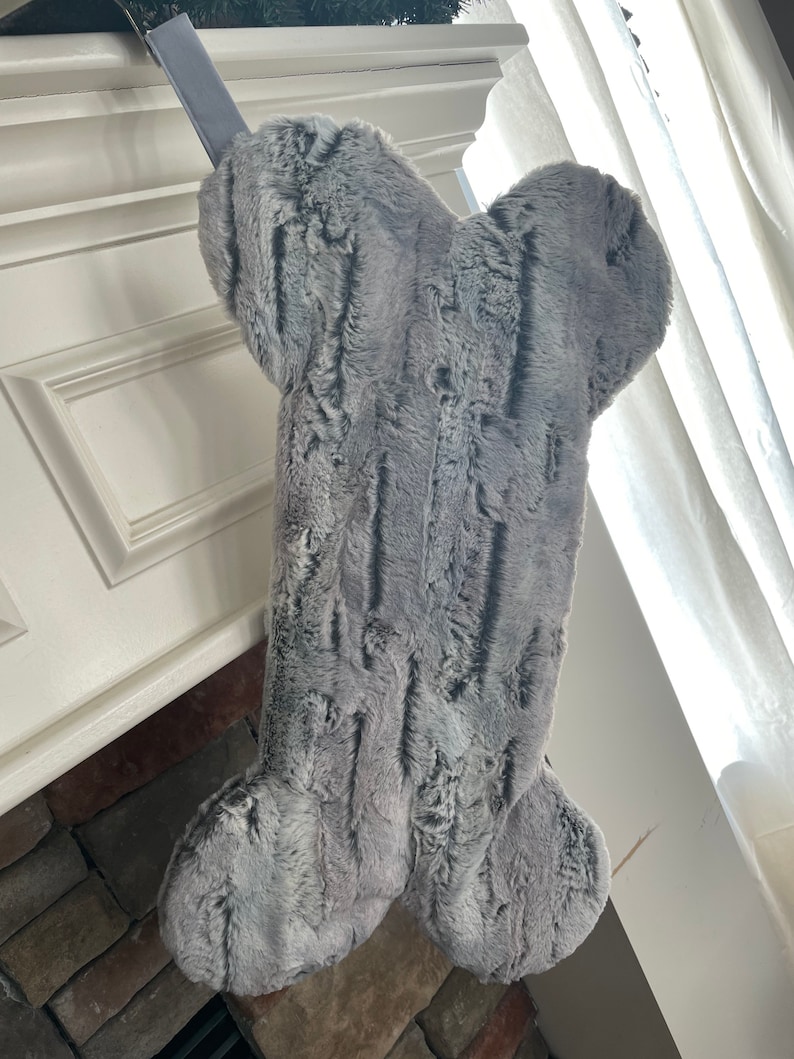May include: A gray faux fur dog bone stocking hanging on a fireplace mantel.