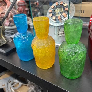 May include: Three glass bottles with textured surfaces. The bottles are blue, yellow, and green.