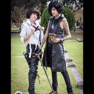 May include: Two people dressed in cosplay costumes. One person is wearing a white jacket, black pants, and boots. The other person is wearing a black leather jacket, black pants, and boots. They are both holding props.