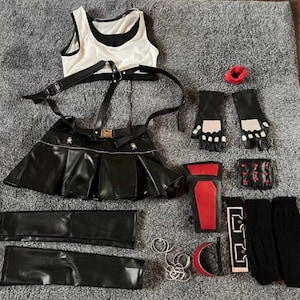 Könnte beinhalten: Ein schwarz-weißes Cosplay-Outfit mit einem plissierten Rock, Handschuhen und Armbändern. Zubehör umfasst ein rotes Armband, Ringe und einen kleinen roten Gegenstand. Das Outfit ist auf einer grauen Oberfläche angeordnet.