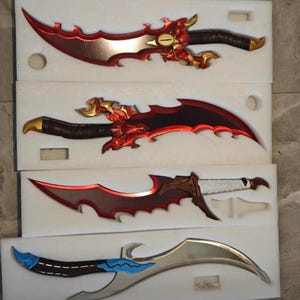 May include: Four decorative fantasy knives with ornate designs. The blades are red, silver, and brown, with intricate handles in gold and black. The knives are displayed in a white foam insert.