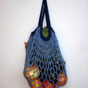 May include: A blue crocheted mesh bag filled with produce, including oranges, avocados, and onions. The bag is hanging on a white wall.