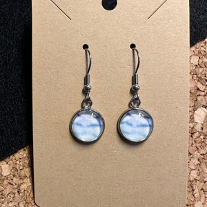 May include: A pair of silver dangle earrings with round glass charms featuring a white and blue watercolour design.