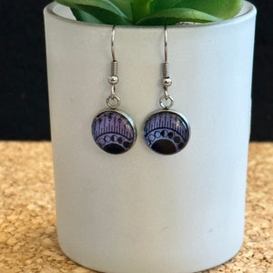 May include: A pair of silver dangle earrings with purple and black glass cabochons featuring a crescent moon and stars design.