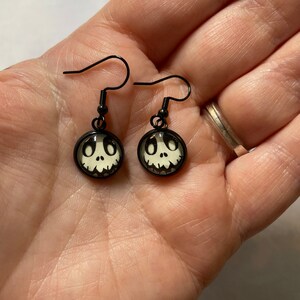 May include: A pair of black dangle earrings with a white Jack Skellington face on each earring.