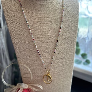 May include: A white beaded lanyard with a gold clasp and a gold ring. The beads are multi-colored and include red, green, and black.
