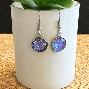 May include: A pair of silver dangle earrings with round purple and blue glitter resin cabochons.