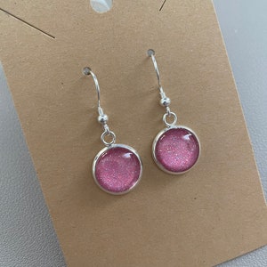 May include: A pair of silver dangle earrings with pink glitter round cabochons.