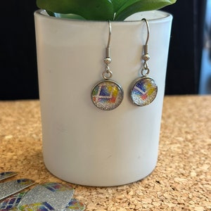 May include: A pair of silver dangle earrings with round, colourful, glittery, glass charms. The charms have a geometric pattern.