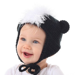 May include: A baby wearing a black and white crocheted skunk hat with a white pom-pom on top.