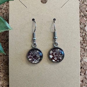 May include: A pair of silver dangle earrings with round, clear glass charms. The charms have a glittery, iridescent finish with a mix of silver and pink glitter.