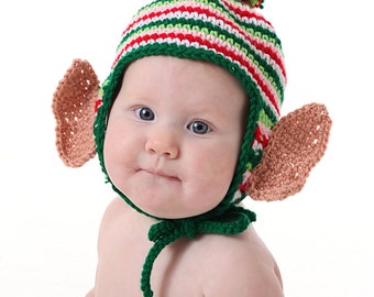 May include: A baby wearing a green, red and white striped elf hat with a pink pom-pom on top. The hat has brown crocheted ears.