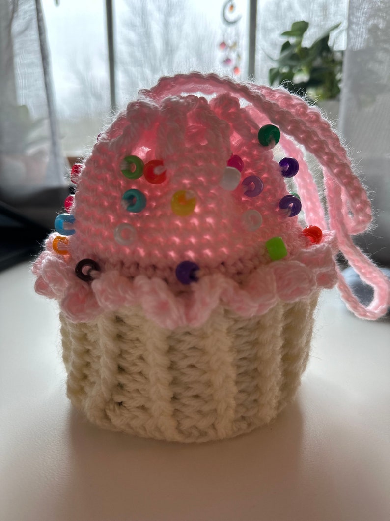 Peut inclure: Un coussin &agrave; &eacute;pingles en forme de cupcake crochet&eacute; avec un gla&ccedil;age rose et un moule &agrave; cupcake blanc. Le coussin est d&eacute;cor&eacute; de perles color&eacute;es.
