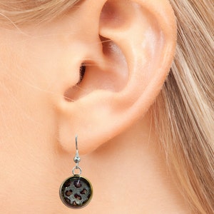 May include: Silver dangle earrings with a round, clear, glass charm featuring a brown and white leopard print.