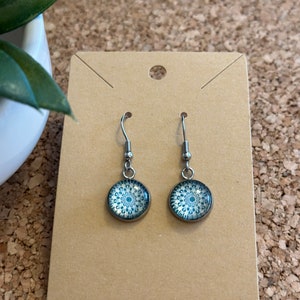 May include: A pair of silver dangle earrings with a blue and white mandala design on the circular pendant.