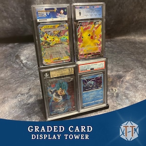 May include: A black graded card display tower holding four encased trading cards. The cards feature colorful illustrations of characters, including Pikachu. The tower has a dark base and clear acrylic card holders.